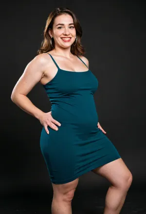 3/4 side view, Curvy gilf, looking at viewer, eye contact, portrait photo a ssbbw mature 60 year old woman, wearing a v-neck sleeveless spaghetti strap green dress, hourglass figure, huge hips, large waist, narrow waist, thighs, saddlebags, round face, chubby cheeks, wrinkles, flushed cheeks, double chin, big eyes, long hair, brunette hair with highlights, medium hair, big smile, mouth open, lips parted, big lips, teeth showing, perfect teeth, joyful smile, (solid blank black background), pokies, hoop earrings, (wrinkles), hard nipples, huge ass, mew2bodi, her, upper, body, is, slim, and, small, chest, while, lower, extra, curvy, wide, big, hips, thick, legs, round, Her, completely, flat-chested, with, no, hint, of, curvature, paired, a, chubby, abdomen, that, accentuates, sleek, angular, frame., This, stark, minimalism, contrasted, by, outrageously, exaggerated, so, impossibly, they, dominate, silhouette, are, immensely, powerful, dramatically, curvaceous, creating, an, extreme, striking, imbalance., <lora:mew2bodi:.2>