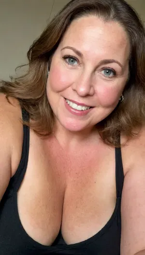 Photo of a fat 60 year old mature brunette woman with beautiful eyes, ((obese)), realistic skin, skin texture visible, (sharp focus), (high quality), (face visible), ((Detailed Face and Eyes)), 8k high definition, ((old woman)), long hair, ((light brunette hair)), ((chubby woman)), ((sexy woman)), ((black thin low-cut v-neck t-shirt)), ((smiling)), close up, ((leaning towards viewer)), ((saggy)), ((cleavage)), ((pokies)), ((erotic background)), (((perfect lighting))), ((front view)), (((looking at viewer))), (((chubby face:1.3))), (((round face:1.3))), ((mature woman)), (detailed skin texture, skin imperfections), (age-appropriate skin condition, wrinkles, wrinkled skin), downblouse, nipslip, stretch, marks, puffy, nipples, dark, ghost, wide, <lora:add-detail-xl:.8>, <lora:RealDownblouseXL2:1>, <lora:stretch_marks:.8>, <lora:Nipples XL:.8>