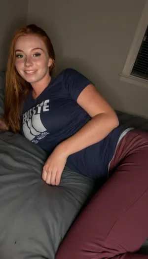 Amature candid photo, Amature 21 year old athletic beauty, long ginger hair, laying on her side next to you on a bed, dark dorm room, wearing sweatpant pjs and a tight tshirt, cleavage, small flirty smile, ultimate realism, poor lighting, at night, dark, night, realistic detailed skin texture, focus on realistic face, Sun-kissed skin