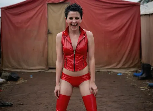 pale 39yo woman, very short spiky black hair, very small tiny breasts, ((full frontal nude, full body)), (glossy red pvc vest and high red pvc boots), in african refugee camp, laughing, freckles