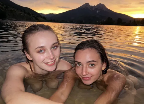 Candid photo, stunning naked 21 year old, saggy droopy boobs, athletic body, small smile, realistic detailed eyes, Swimming in a small clear mountain lake with her unique friend, she is mostly submerged, vivid sunset, golden hour, scenic, realistic detailed face, realistic detailed skin